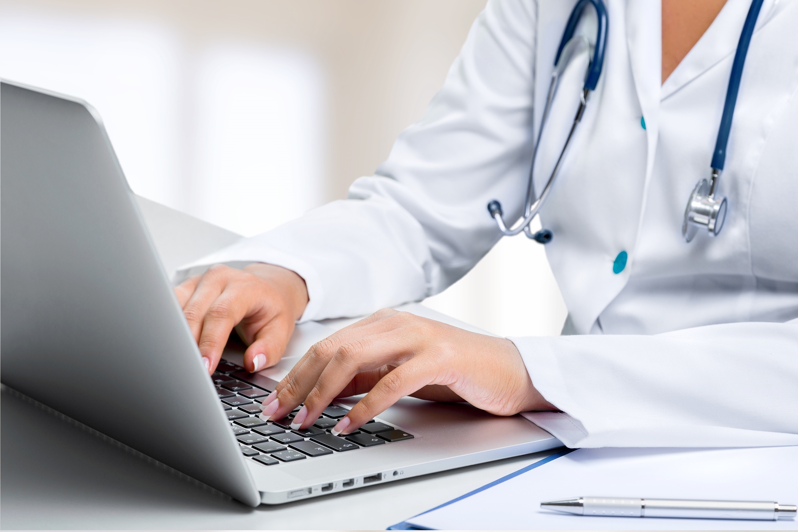 photo of doctor sitting in front of laptop with hands on keypad