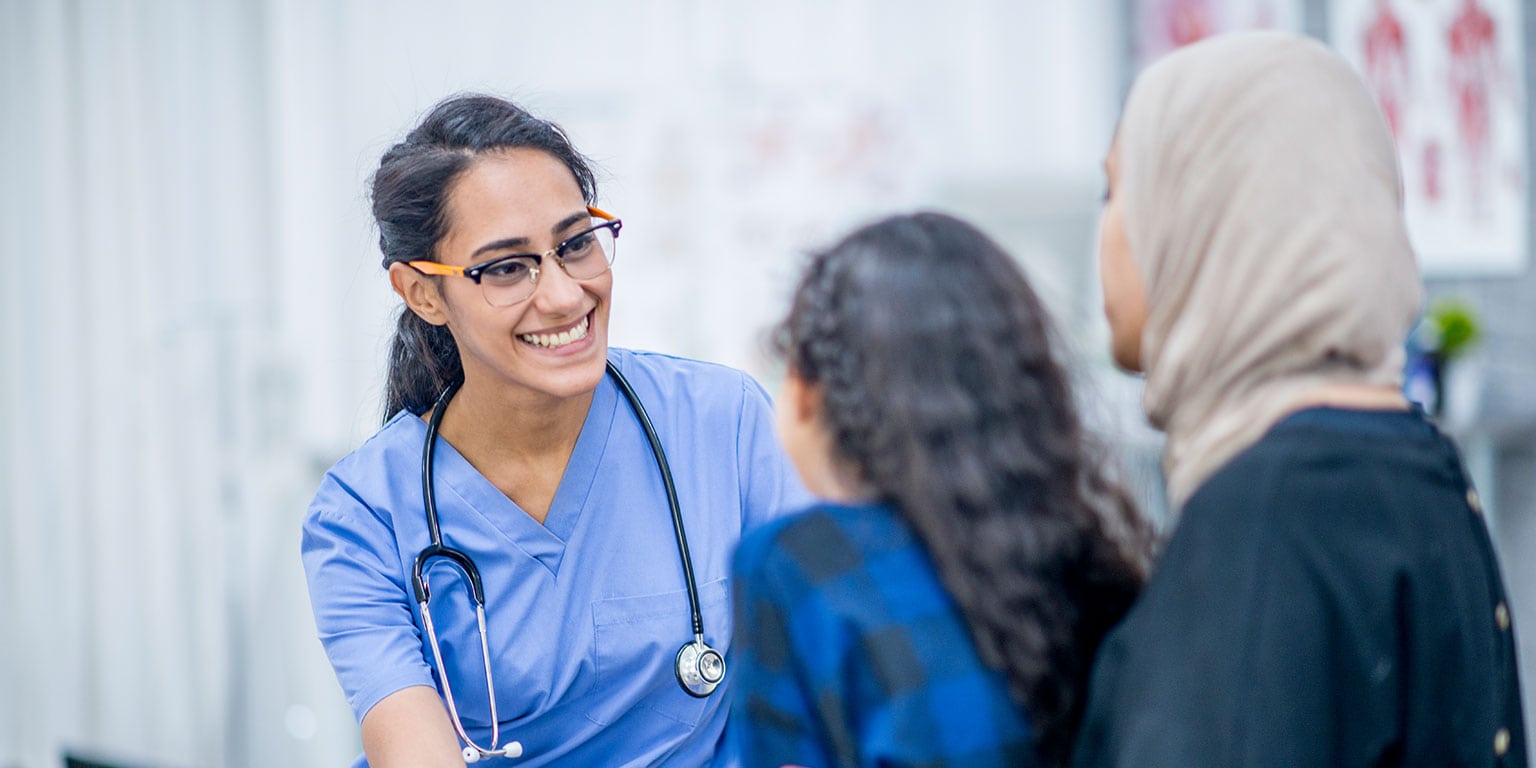 Nurse smiling at young girl sitting on mothers lap